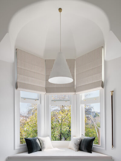 Bay window seat with striped Roman blinds, white walls, and soft cushions in an Australian home.