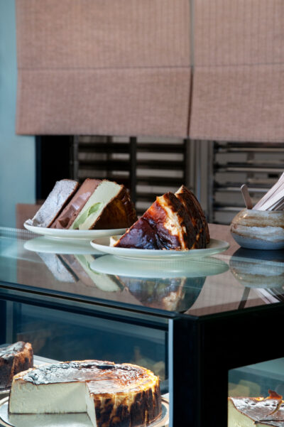 Plates of cheesecake slices on café counter with neutral linen blind in Hawthorn café.