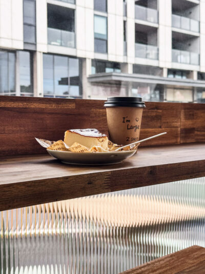 Coffee cup and cheesecake on timber window bench inside Better Burnt Hawthorn café.