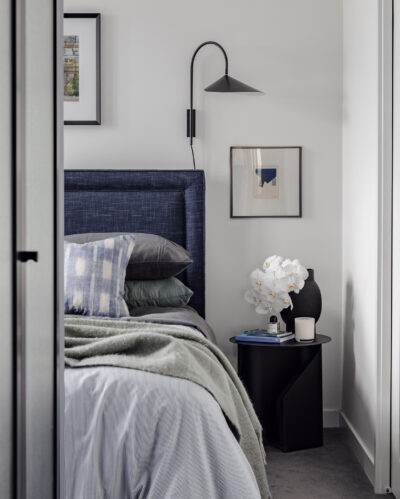 Bedroom with upholstered blue headboard, layered bedding, and black wall sconce in Collingwood apartment.