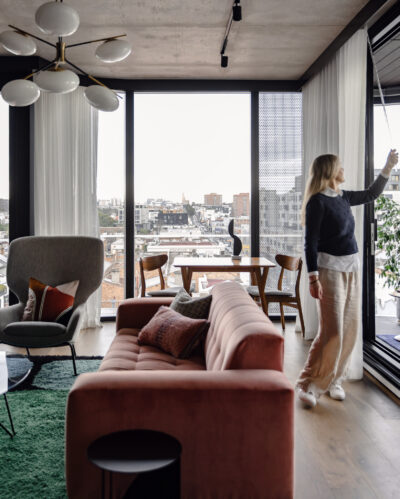 Living room with pink velvet sofa, modern armchair, and city views in Collingwood apartment.
