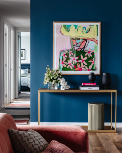 Living room with deep blue wall, bold artwork, console table, and pink velvet sofa in Collingwood apartment.