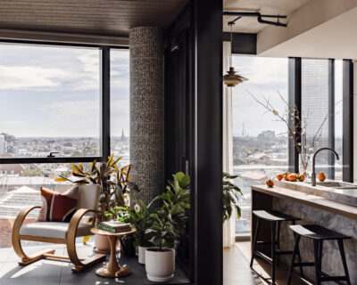 Open-plan kitchen and winter garden with tiled column, armchair, and marble island in Collingwood apartment.