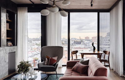 Open-plan living room with pink sofa, armchair, dining table, and city views in Collingwood apartment.