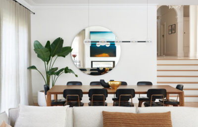 Contemporary dining room with large round mirror, timber table, and statement lighting.