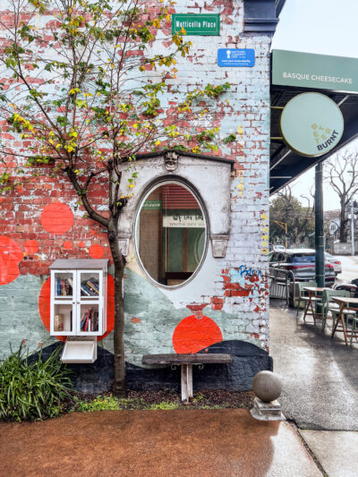 Street art brick wall with oval window, tree, and Better Burnt café sign in Hawthorn.