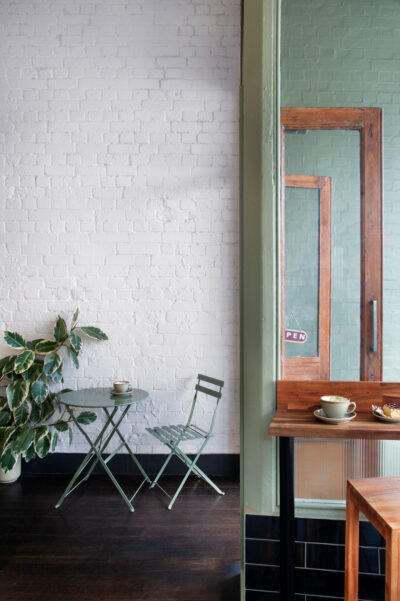 Green café table and chair against whitewashed brick wall with coffee cup inside Better Burnt Hawthorn.