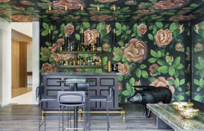 Luxury home bar with bold floral mosaic wall, black cabinetry, and brass accents.