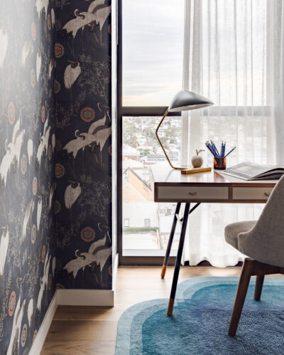 Guest bedroom with patterned wallpaper, timber desk, and blue rug in Collingwood apartment.