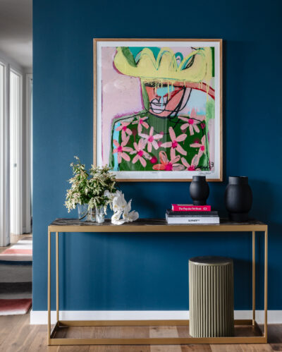 Hallway view with framed artwork on deep blue wall and console table in Collingwood apartment.