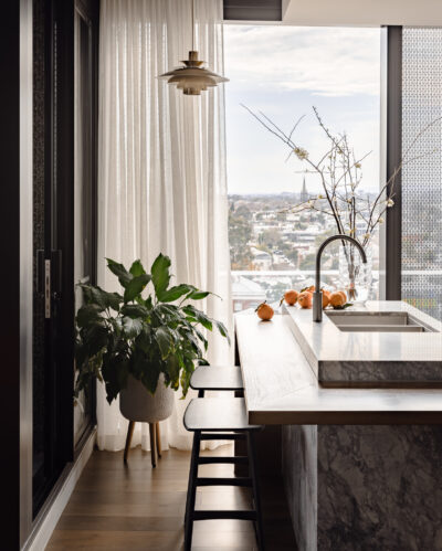Marble kitchen island with sink, pendant lighting, and floor-to-ceiling curtains in Collingwood apartment.