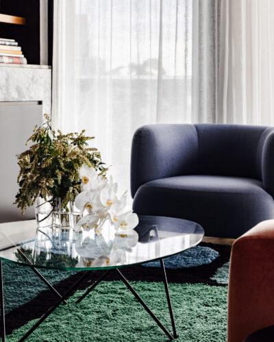 Blue armchair and glass coffee table with floral arrangement in Collingwood apartment living room.