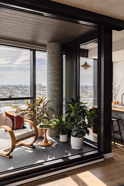 Indoor winter garden with timber armchair, potted plants, and expansive city views in Collingwood apartment.