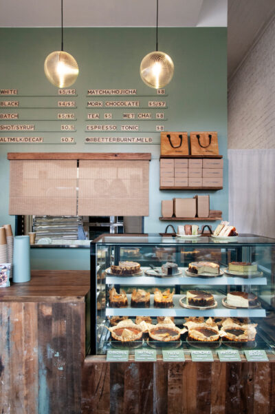 Café menu on sage green wall with pendant lights and display counter at Better Burnt Hawthorn.