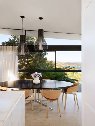 Australian dining room with round timber table, sculptural pendant lights, and coastal views.