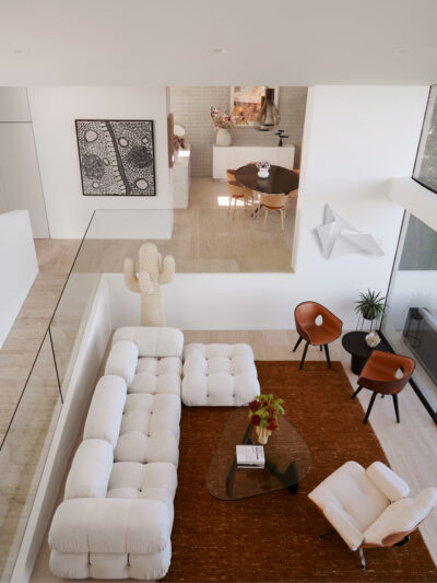 Open-plan Australian home with white sectional sofa, leather chairs, and contemporary art.