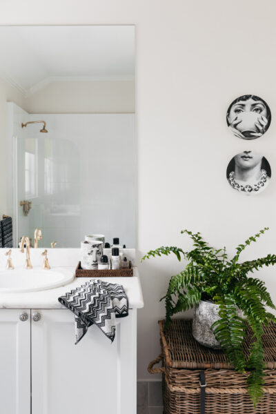 Bathroom with marble vanity, brass tapware, black and white decor, and indoor plant.