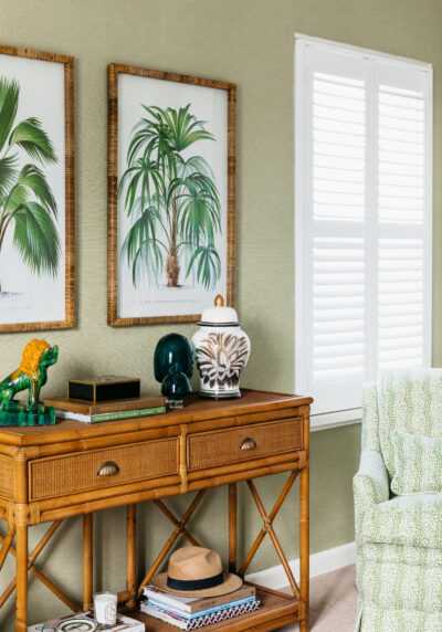 Bedroom with rattan console, framed botanical prints, and green upholstered armchair.