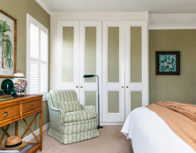 Bedroom with patterned green armchair, rattan console, and botanical prints.