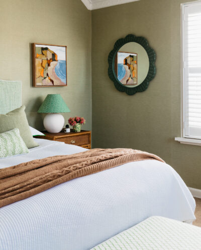 Bedroom with green wallpaper, brown throw, and modern coastal artwork.