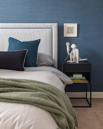 Bedroom with blue wallpaper, striped upholstered headboard, and bedside table styling.