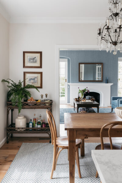 Dining space with timber table, rattan bar cart, and chandelier in Toorak home.