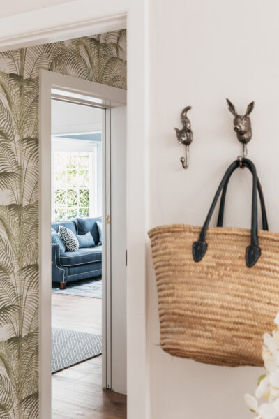 Hallway with palm wallpaper and view into blue living room with patterned sofa.