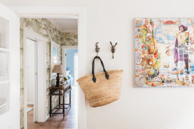 Hallway with tropical wallpaper, rattan console, wall hooks, and colourful artwork.