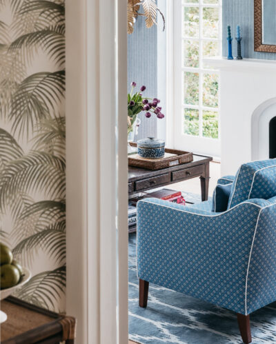 Entry hallway with rattan console, palm wallpaper, and light-filled view to blue living room.