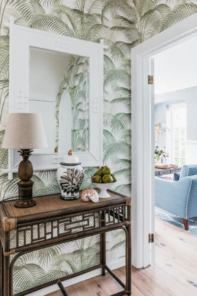 Hallway with palm leaf wallpaper, rattan console, and decorative accents.