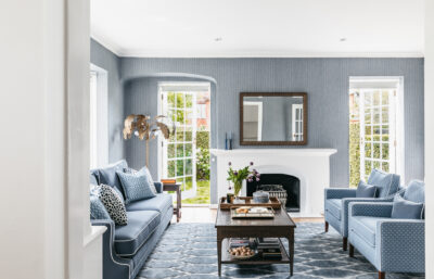 Elegant blue living room with white fireplace and patterned rug in a Toorak heritage home.