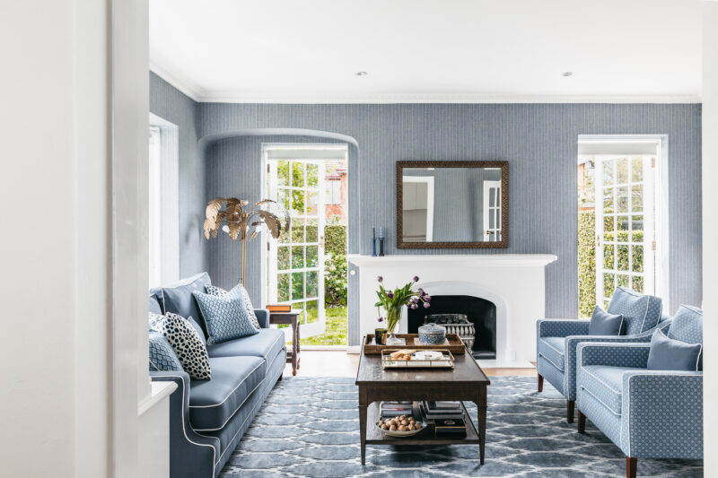 Elegant blue living room with white fireplace and patterned rug in a Toorak heritage home.