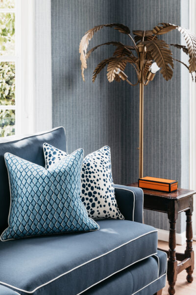 Blue sofa with patterned cushions beside a sculptural gold palm lamp and open French doors.