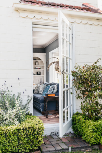 View through open French doors from garden into blue living room with patterned upholstery.