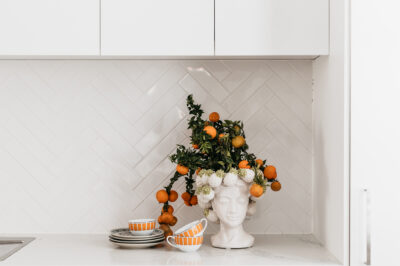 Close-up of white kitchen with citrus arrangement and herringbone tiled splashback.
