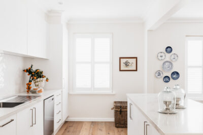 White kitchen with herringbone tiles, marble benchtop, and timber flooring.
