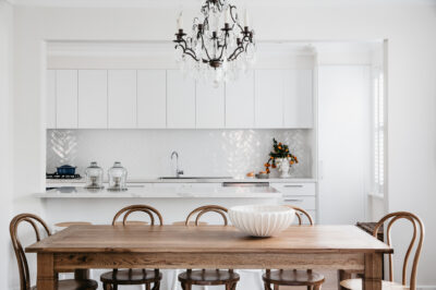 Kitchen with white cabinetry, timber dining table, and crystal chandelier.