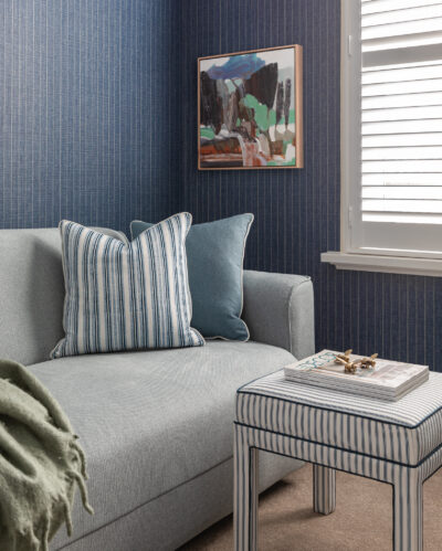 Blue living room with striped wallpaper, sofa, and artwork on wall.