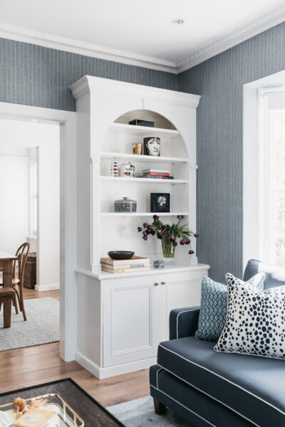 White arched bookshelf styled with ceramics and books against blue wallpaper.
