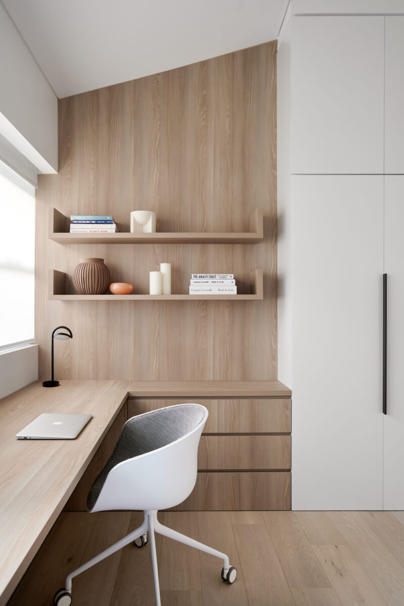 Minimalist home office with warm timber panelling, floating shelves, and sleek white chair.