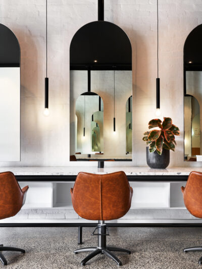 Luxury beauty salon interior designed by The Stylesmiths with arched mirrors, marble styling stations, warm leather salon chairs and contemporary boutique interiors.